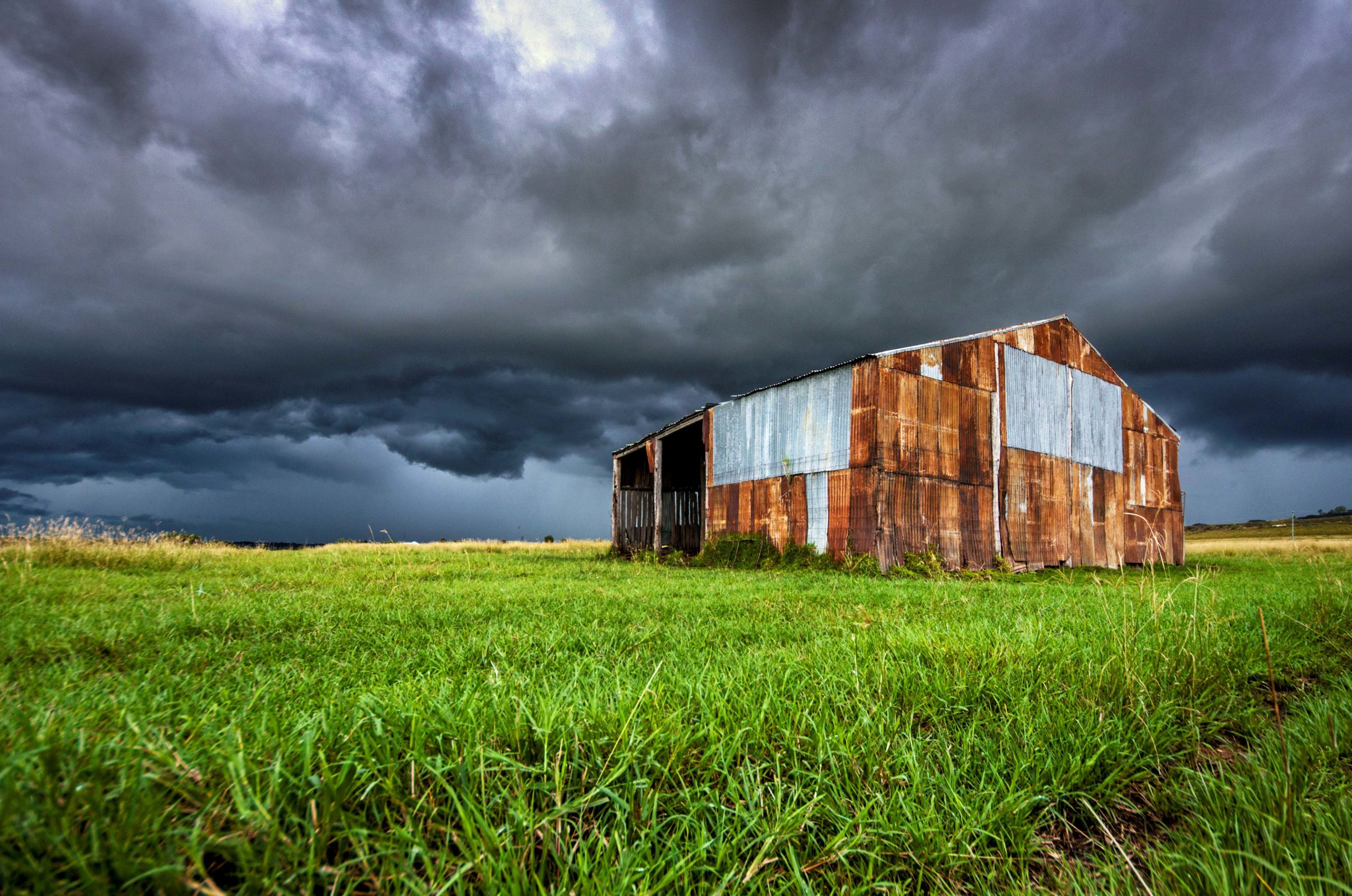 An old tin farm shed stands in a field while a storm brews in the distance.